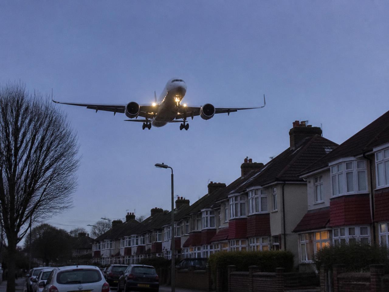 Passenger jet on final approach at dusk, low over a suburban street of semi-detached houses